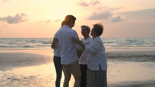 Rear view of man standing on beach against sky during sunset