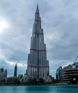 Burj khalifa by lake against cloudy sky