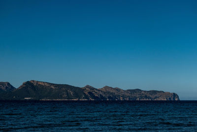 Scenic view of sea and mountains against clear blue sky