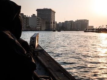 Rear view of person in river against cityscape during sunset