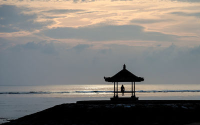 Silhouette lifeguard hut on beach against sky during sunset