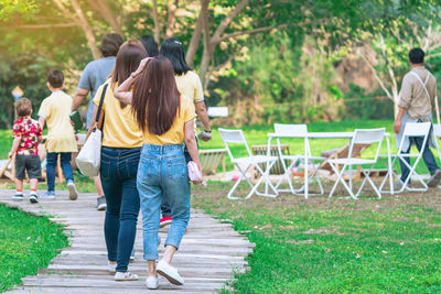 Back view of asian woman walking on pathway through  garden.  people walking together in park. 
