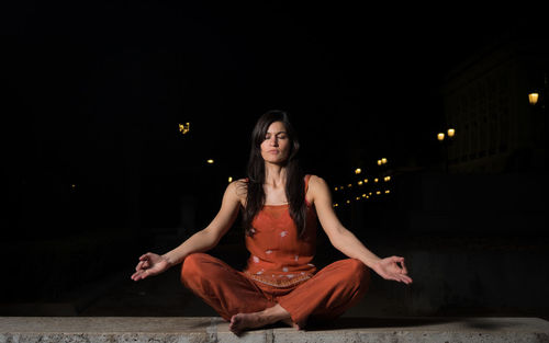 Young woman sitting against black background