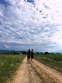 Rear view of friends walking on road against cloudy sky