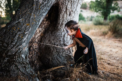 Side view of man holding tree trunk in forest