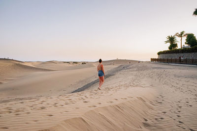 Rear view of woman walking at beach against clear sky