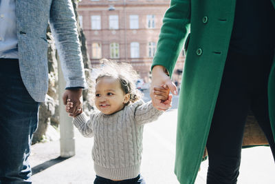 Happy girl walking with midsection of parents in city