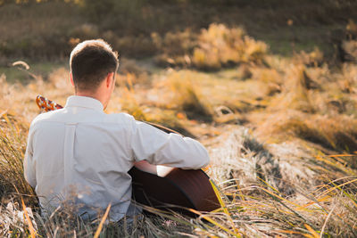 Man with acoustic guitar sits in the autumn grass, tranquil scene