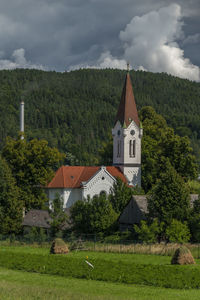 Built structure by trees and buildings against sky