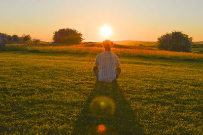 Rear view of man on field against sky during sunset