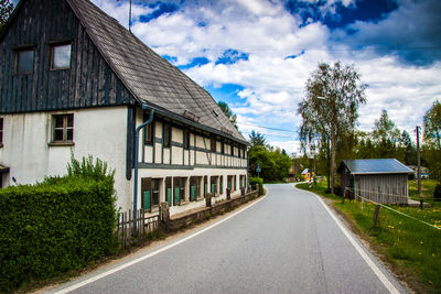 Road amidst trees and buildings against sky