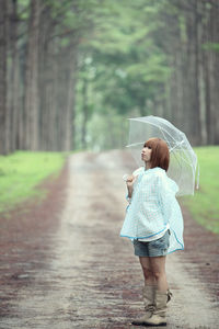 Side view of woman with umbrella standing on road against trees in forest