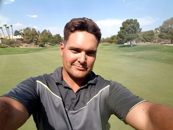 Portrait of confident golfer standing on grassy field against sky