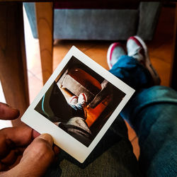 Low section of man holding instant transfer print while sitting at home