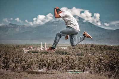 Full length of man jumping on field against sky