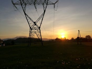 Silhouette electricity pylon on field against sky during sunset