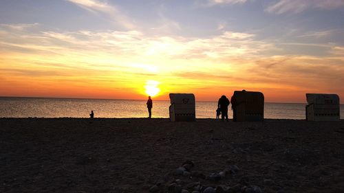 Silhouette people on beach against sky during sunset