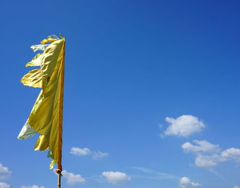 Low angle view of yellow flag against blue sky