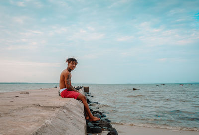 Woman sitting on shore at beach against sky