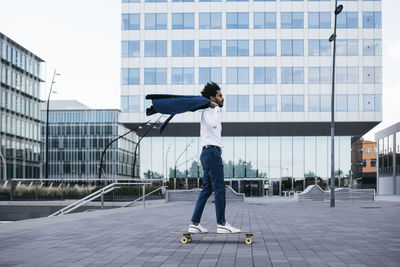 Spain, barcelona, young businessman riding skateboard in the city