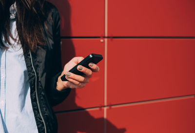 Midsection of woman using mobile phone against red wall