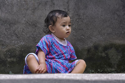 Cute girl looking away while sitting on wall