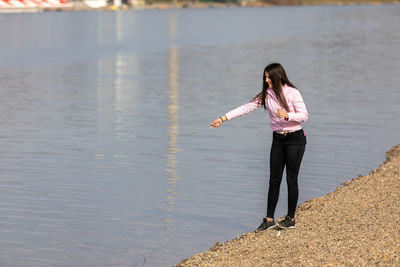 A young girl standing on the lake bank and throwing stones into the water. recreation in nature