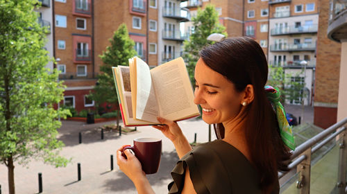 Smiling young woman holding coffee cup and book