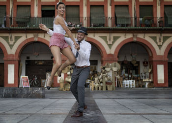 Happy couple dancing on footpath against building in city