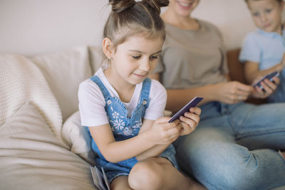 Cute girl using mobile phone while sitting on sofa