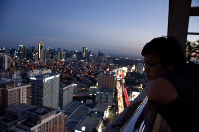 Side view of young man looking at illuminated cityscape through window at home