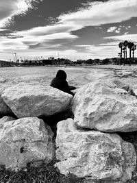 Rear view of men sitting on rock at beach against sky