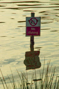 Close-up of information sign on wooden post in lake