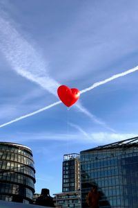 Low angle view of heart shape red balloon against sky in city