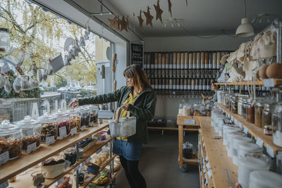 Mature woman shopping groceries from glass jar in zero waste shop