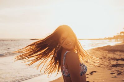 Rear view of woman standing at beach against sky during sunset