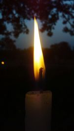 Close-up of illuminated candle against sky at sunset