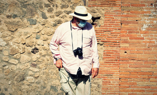 Man wearing hat standing against brick wall