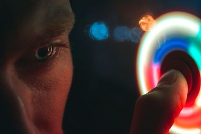 Close-up of young man spinning illuminated fidget spinner at night