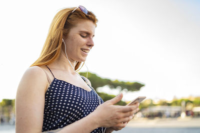 Cheerful woman listening to music and using smartphone
