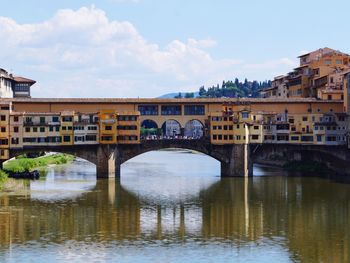 Arch bridge over river by buildings against sky