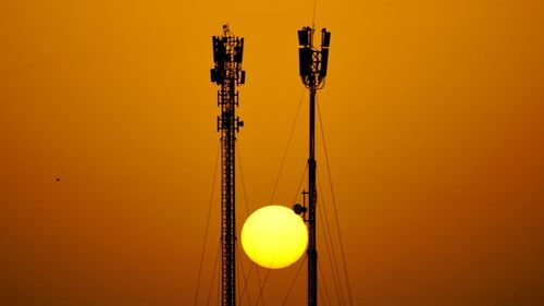 Low angle view of communications tower against orange sky