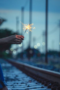 Cropped hand holding sparkler by railroad track
