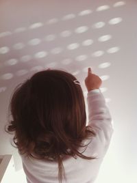 Rear view of girl touching sunlight pattern on white wall