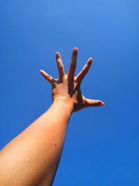 Cropped image of hand reaching against clear blue sky