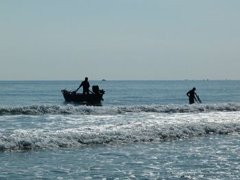 Silhouette people in sea against clear sky