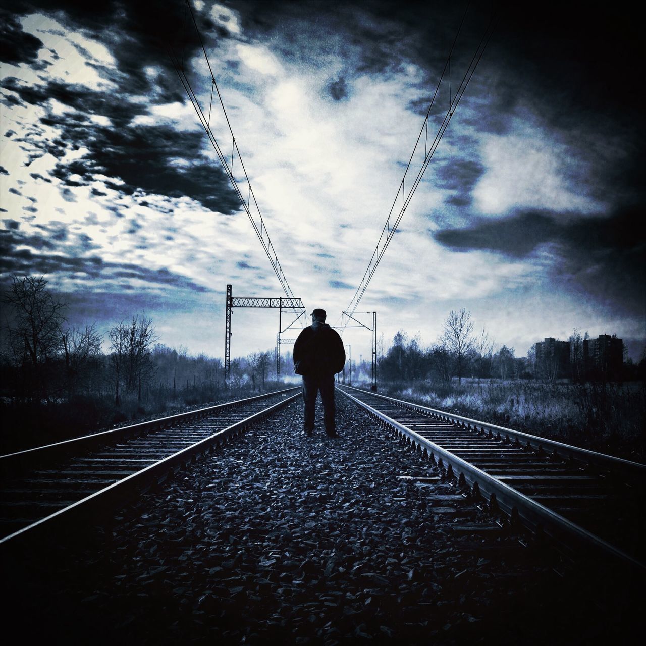 railroad track, rear view, the way forward, sky, rail transportation, full length, standing, diminishing perspective, transportation, cloud - sky, walking, lifestyles, vanishing point, connection, men, cloud, power line, leisure activity