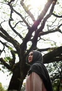 Low angle view of woman standing on tree against sky