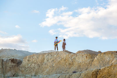 Rear view of woman standing on rock against sky