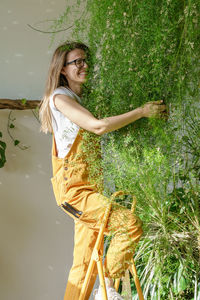 Joyful woman gardener standing on stepladder hugging lush asparagus plant at flower store. hobby